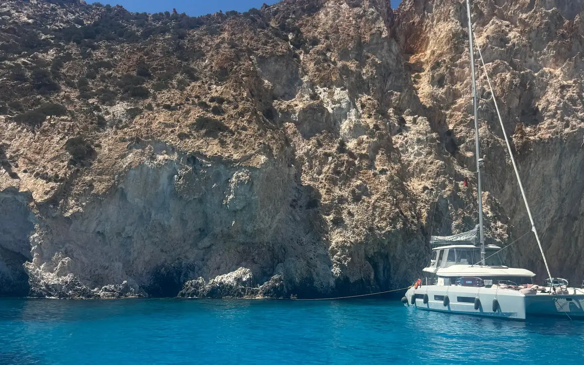 Un catamaran blanc sous des falaises volcaniques grises et brunes