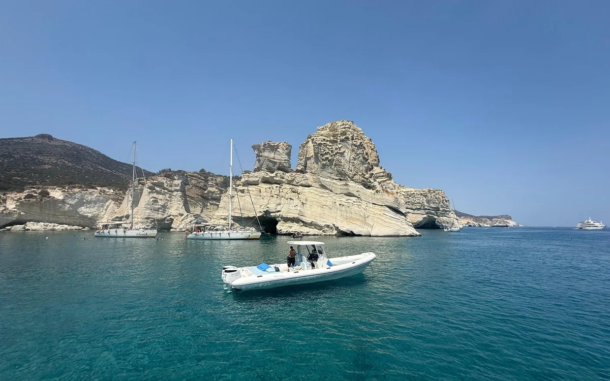 Ein weißes Motorboot auf blau-grünem Wasser, zwei Segelboote unter einem hohen weißen Felsen dahinter