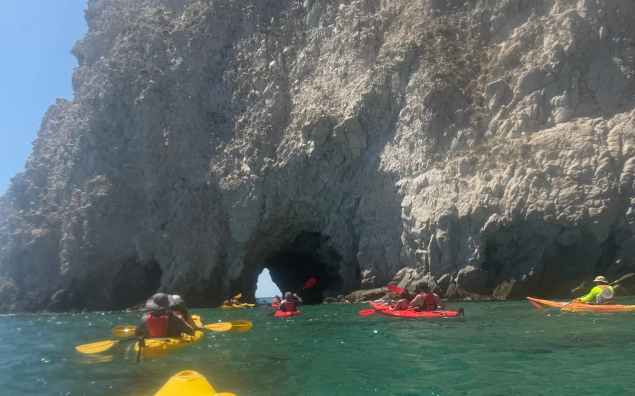 Kayakistes pagayant au pied d'une falaise sombre avec une ouverture de grotte