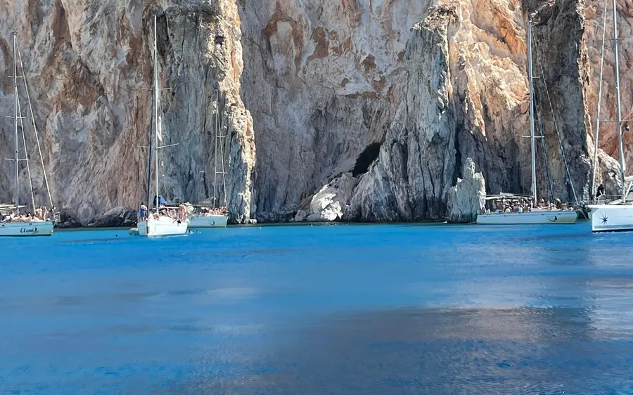 Boote ankern unter hohen, gestreiften Klippen über tiefblauem Wasser