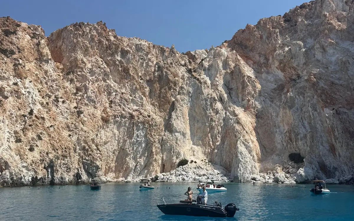 Petits bateaux à moteur et nageurs dans une crique bleue sous des falaises abruptes blanches et couleur rouille