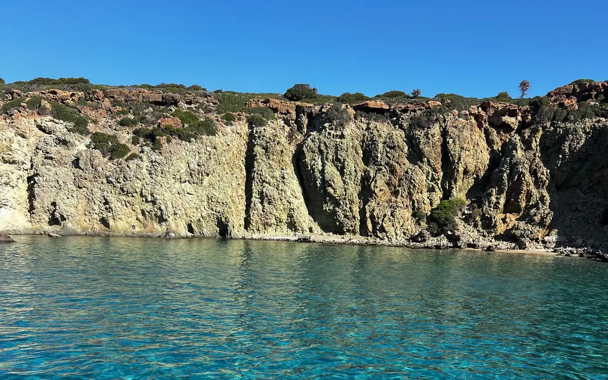 Hauts-fonds turquoise sous une falaise de roche ocre et grise coiffée de broussailles vertes